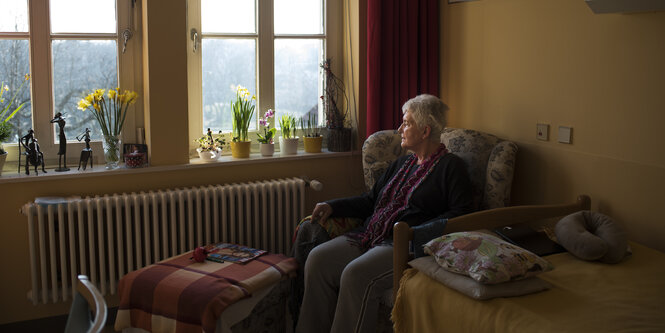 Eine ältere Frau sitzt auf einem Sessel und schaut aus dem Fenster