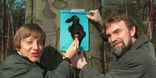 Jochen Flasbarth steht mit Angela Merkel vor einem Baum und hält ein Plakat fest, während sie darauf herumpinselt