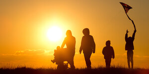 Eine Familie mit Kinderwagen und einem Drachen an der Schnur geht bei Sonnenuntergang über einen Weg durch die Salzwiesen im Watt bei Westerhever