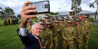 Ein Mann in Anzug macht ein Selfie von sich und einer Gruppe uniformierter Soldaten