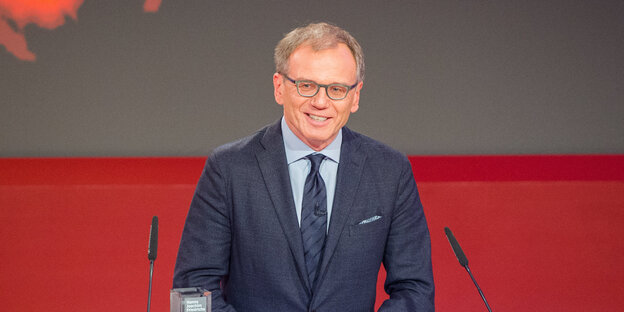 Armin Wolf steht lächelnd hinter zwei Mikrofonen Armin Wolf steht lächelnd hinter zwei Mikrofonen