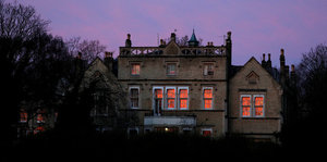 Ein Haus, in dessen Fensterscheiben sich der Sonnenuntergang spiegelt, dahinter violetter Himmel