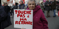 Eine ältere Frau trägt bei einer Demo in Paris ein Schild mit der Aufschrift "Hände weg von meiner Rente"