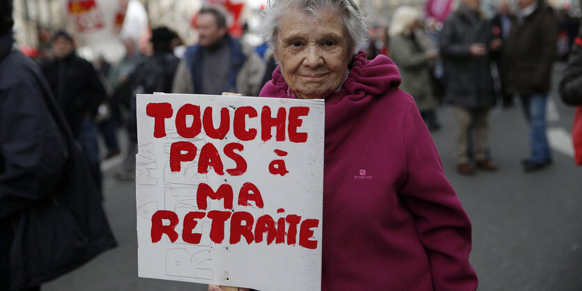 Eine ältere Frau trägt bei einer Demo in Paris ein Schild mit der Aufschrift "Hände weg von meiner Rente"