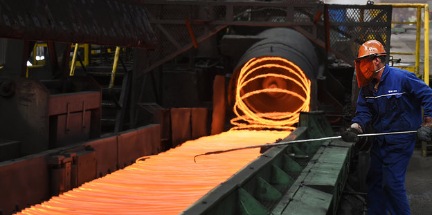Ein Mann in einem Blaumann arbeitet mit flüssigem Stahl, der orange glüht
