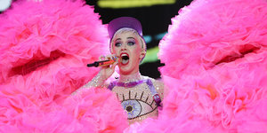 Katy Perry singt in ein Mikrofon, neben ihr rosafarbene Stoffberge