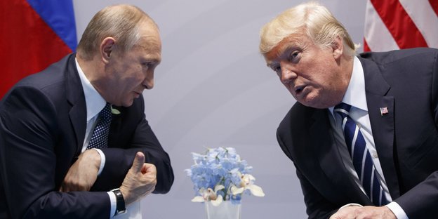 Putin und Trump sitzen an einem Tisch und lehnen sich aufeinander zu