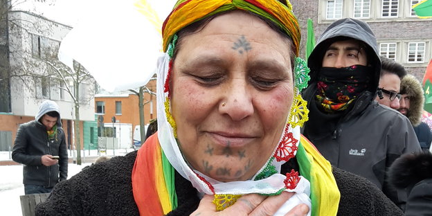 Ältere Frau mit grün-gelb-roter Kopfbedeckung und Gesichtsbemalung
