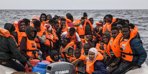 Viele Menschen sitzen in orangen Rettungswesten in einem überfüllten Schlauchboot