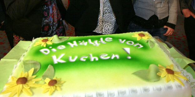 Eine Torte mit grünem Farbstoff und Sonnenblumen aus Zuckerguss. Auf der Torte steht: "Die Hälfte vom Kuchen".
