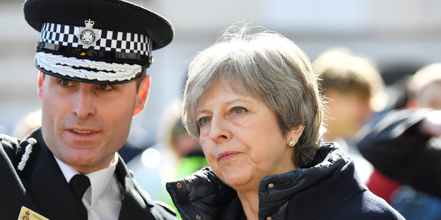 Ein Mann in Polizeiuniform und eine Frau mit kurzen, grauen Haaren schauen zur linken Seite des Fotos