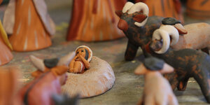 In einer Krippe liegt ein kleiner Jesus aus Lehm zwischen Schafen aus Lehm