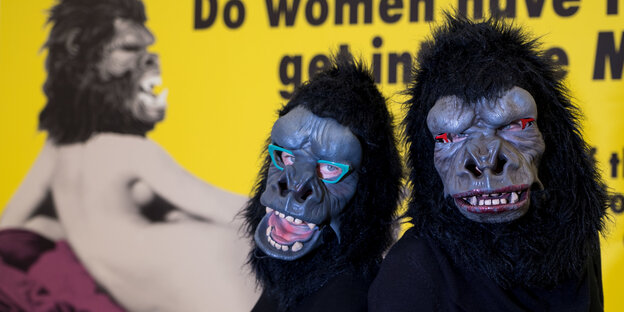 Vor einem gelben Plakat stehen zwei Menschen mit Gorilla-Masken
