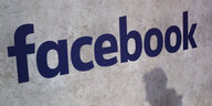 Der Schriftzug "facebook" an einer Wand, darunter der Schatten eines Mannes