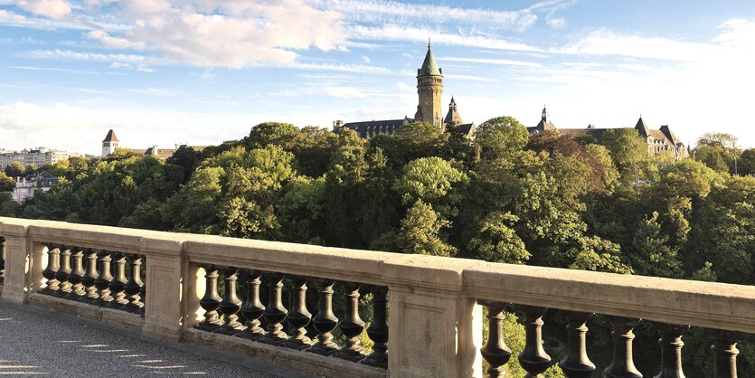 Blick auf eine Balustrade, dahinter erhebt sich ein bewaldeter Berg mit Turm