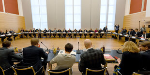 Viele Menschen in Anzügen sitzen in einem großen Kreis.