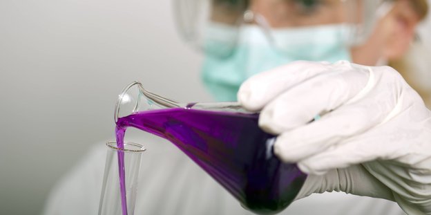Wissenschaftlerin gießt eine lilafarbene Flüssigkeit aus einem Kolben