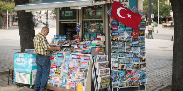Ein Mann steht vor einem Kiosk, an dem eine türkische Flagge weht