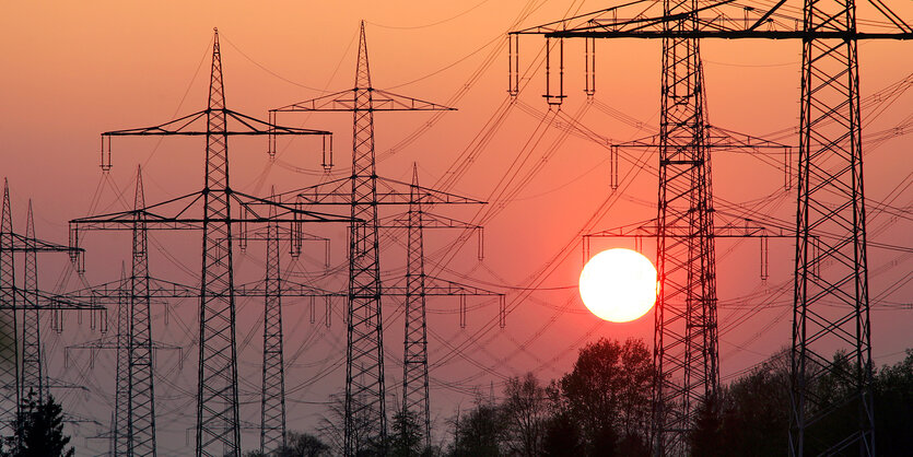 Hinter Hochspannungsmasten geht die Sonne unter