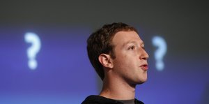 Mark Zuckerberg redet, hinter ihm sind zwei Fragezeichen an einer Wand zu sehen