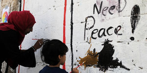 Eine Frau und ein Kind malen während einer Kunstaktion Gaffiti an eine Wand an der "Need Peace!"