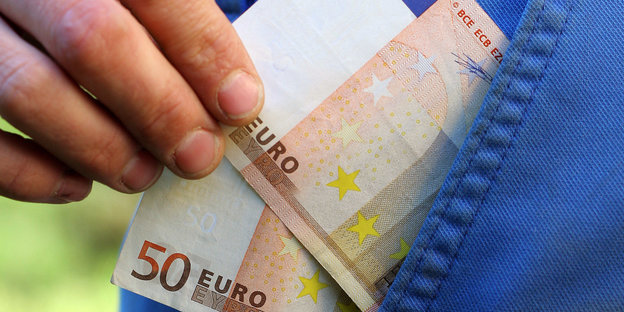 Ein Hand zieht zwei 50-Euro-Scheine aus einer Hosentasche.