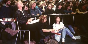 Viele Studierende in einem Hörsaal, ihre Frisuren und Klamotten sehen nach den 80er Jahren aus