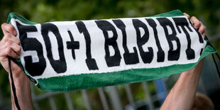 Zwei Hände halten ein Banner mit der Aufschrift "50+1 bleibt"