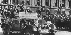 Eine Schwarz-Weiß-Fotografie zeigt Adolf Hitler in einem Auto vor einer jubelnden Menge