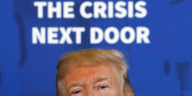 Donald Trump, über ihm steht an einer Wand The Crisis Next Door