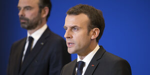 Emmanuel Macron steht vor einer blauen Wand