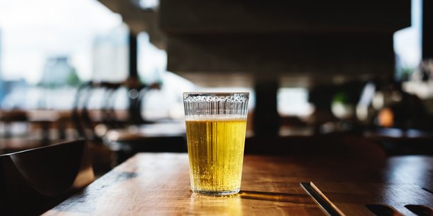 Sonne fällt von hinten durch ein Glas Bier auf einem dunklen Holztisch