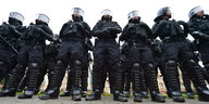 Polizisten in blauen Overalls mit Brustschutz, Schienbeinschutz, Handschuhen und Helmen mit herunter geklapptem Visier.