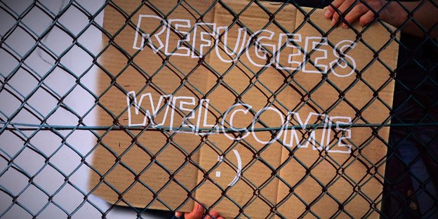 Ein Schild mit „Refugees Welcome“ hinter einem Maschendrahtzaun