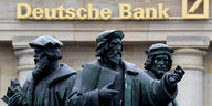 Eine Statue mit drei Männern vor einer Filiale der Deutschen Bank