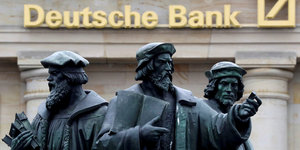 Eine Statue mit drei Männern vor einer Filiale der Deutschen Bank