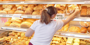 Eine Verkäuferin in einer Bäckerei greift nach dem Brot in einem Regal.