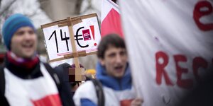 Demonstrierende, einer mit einem Schild auf dem "14 Euro!" steht
