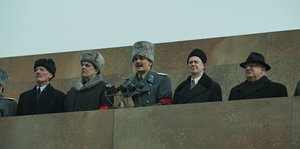 Stalin spricht in ein Mikro. Vier Männer sitzen neben ihm