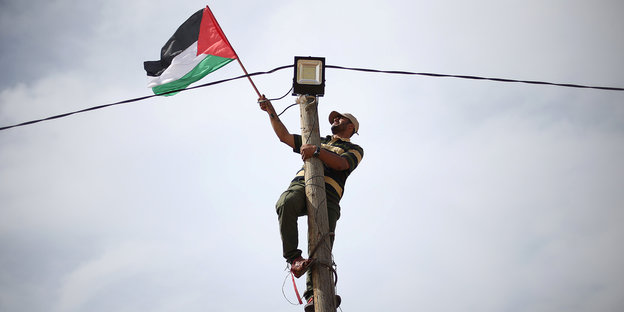 Ein Mann hängt eine palästinensische Flagge auf eine Laterne