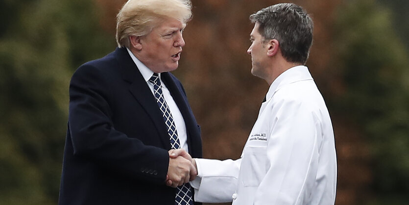 Trump gibt einem Mann in weißem Kittel die Hand.- Es ist Ronny Jackson