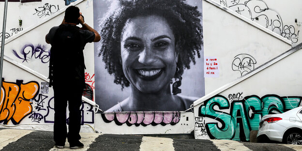 Ein Wandbild mit dem Konterfei von Marielle Franco, davor steht ein Mann und fotografiert