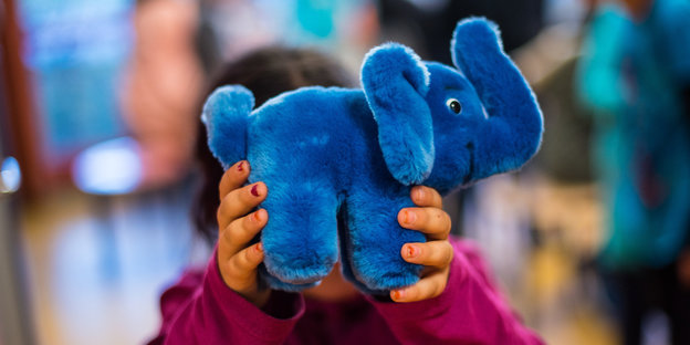 Ein Kind hält einen blauen Elefanten vor sein Gesicht