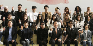 Südkoreanische Popstars, in drei Reihen hintereinander sitzend - alle machen das Victory-Zeichen