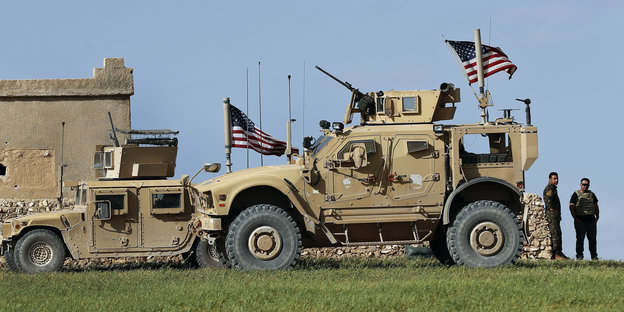 Soldaten stehen neben Militärfahrzeugen über denen US-amerikanische Fahnen wehen