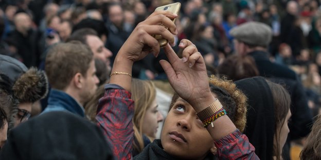 Eine junge Frau macht ein Selfie von sich und eine Demonstration im Hintergrund