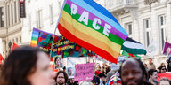Eine Regenbogen-Flage mit der Aufschrift "Pace", getragen von Demonstrierenden
