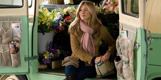 Jennifer Aniston sitzt in einem Auto, in dem viele Blumen stehen