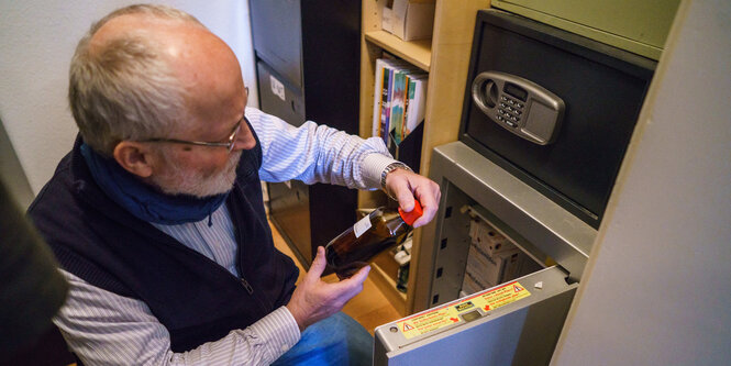 Heinrich Elsner hält vor einem Tresor kniend eine Flasche Methadon in der Hand