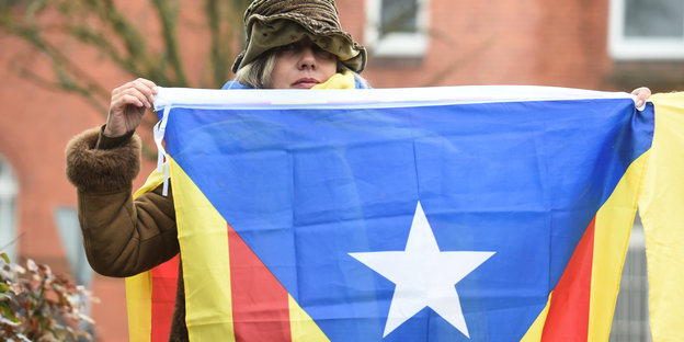 Drei Menschen halten katalanische Flaggen und ein Banner mit der Aufschrift „Seid bitte fair“